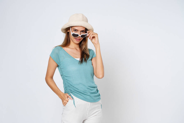 サングラスをかけている若い女性、カラフルな服や帽子、白い背景に隔離されています。ライフスタイルの夏のコンセプト. - 写真・画像