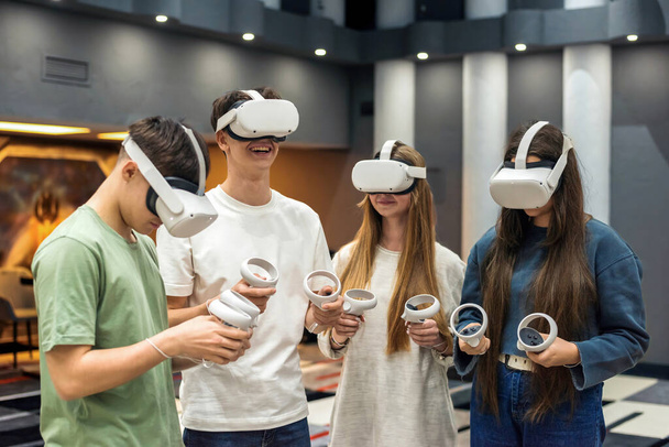 Группа из четырех подростков, взаимодействующих и играющих в игры с использованием оборудования Virtual Reality на арене - Фото, изображение