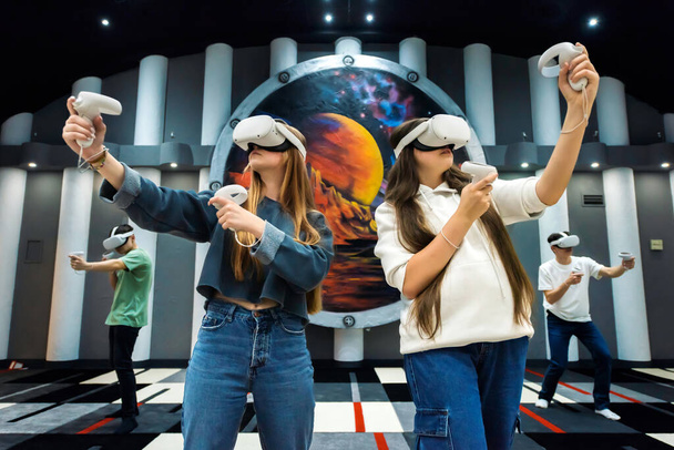 Bir grup arkadaş VR ile etkileşimde. Sanal Gerçekliği kullanarak arenada oynayan bir grup genç. - Fotoğraf, Görsel