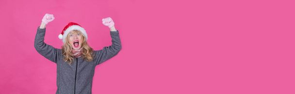 зріла жінка з жестом перемоги в Різдві на рожевому фоні - Фото, зображення