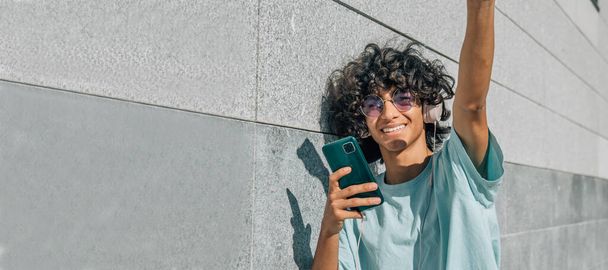 young latin hispanic man with afro hair with headphones and phone in the street - 写真・画像