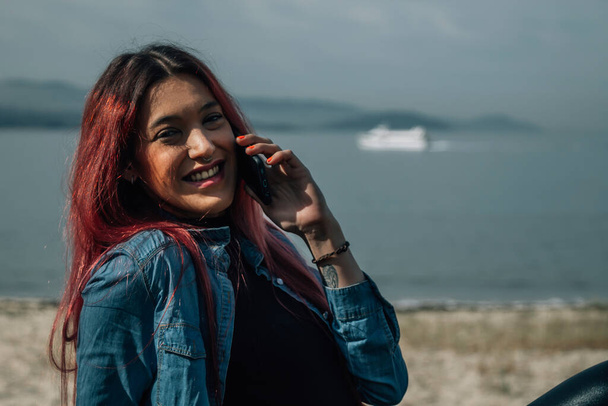 pretty redhead girl with mobile phone in seascape - Zdjęcie, obraz