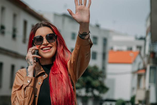 happy young woman with red hair waving and talking on the phone in the street - Photo, Image