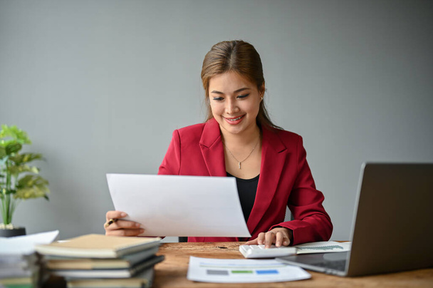 Eine professionelle asiatische Geschäftsfrau aus dem Millennium nutzt einen Taschenrechner, um Budgets zu planen und an ihrem Schreibtisch an Finanzberichten zu arbeiten. - Foto, Bild