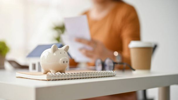 Close-up image of a piggy bank is on table with a female real estate agent working behind. real estate, property investment, realtor, broker, saving, financial, banking, loan - Fotó, kép