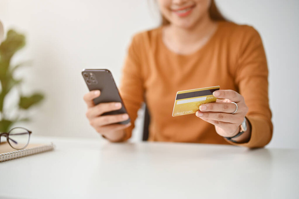 Close-up beeld van een vrouw aangesloten haar creditcard met een shopping app via haar smartphone, geniet van online winkelen thuis. - Foto, afbeelding
