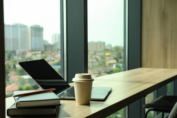 Офісний стіл біля вікна з кавою, ноутбуком і блокнотами
 - Фото, зображення