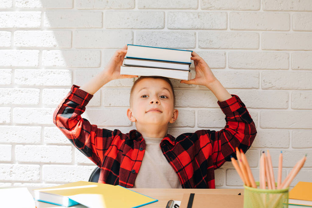 Fogantatás vissza az iskolába. Egy tanuló fiú egy asztalnál ül unigamival, jegyzetfüzetekkel és ceruzákkal. Előnézet - Fotó, kép
