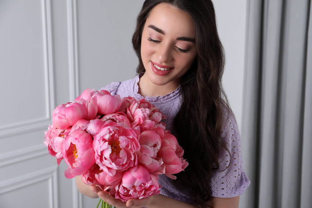 Beautiful young woman with bouquet of pink peonies indoors - Fotó, kép