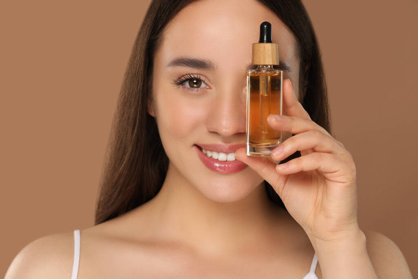 Happy young woman with bottle of essential oil on brown background - Фото, зображення