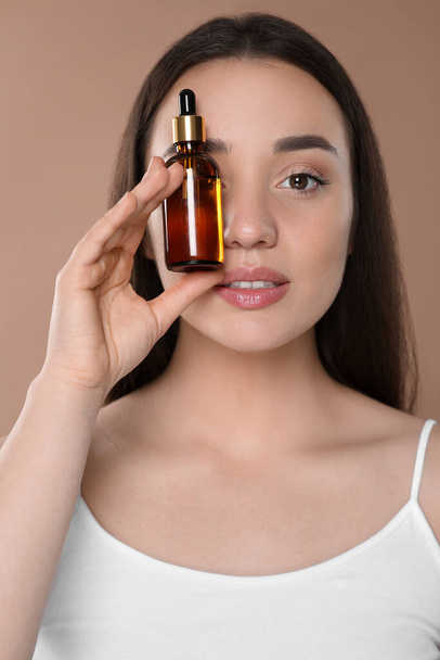 Beautiful young woman with bottle of essential oil on brown background - Fotografie, Obrázek