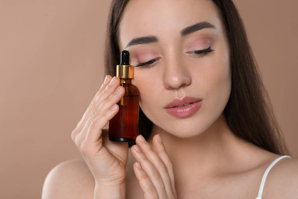 Beautiful young woman with bottle of essential oil on brown background - Foto, afbeelding