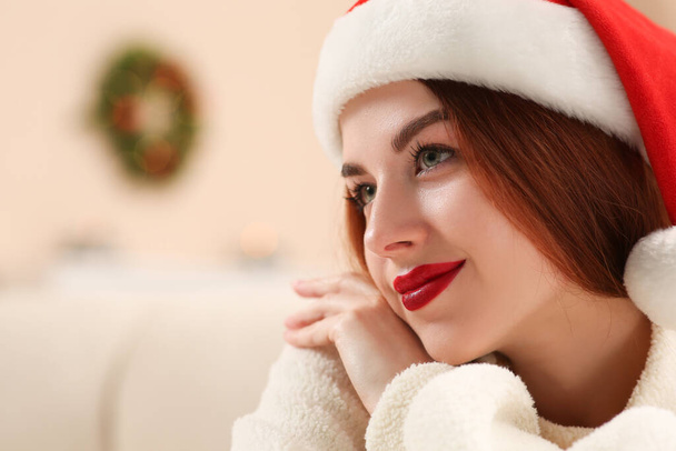 Beautiful young woman in Santa hat on blurred background, space for text. Celebrating Christmas - Fotoğraf, Görsel