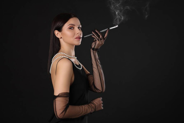 Woman using long cigarette holder for smoking on black background, space for text - Photo, Image