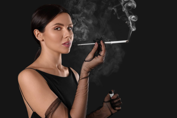 Woman using long cigarette holder for smoking on black background, space for text - Foto, imagen
