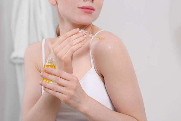 Woman applying essential oil onto shoulder in bathroom, closeup - Foto, Imagem