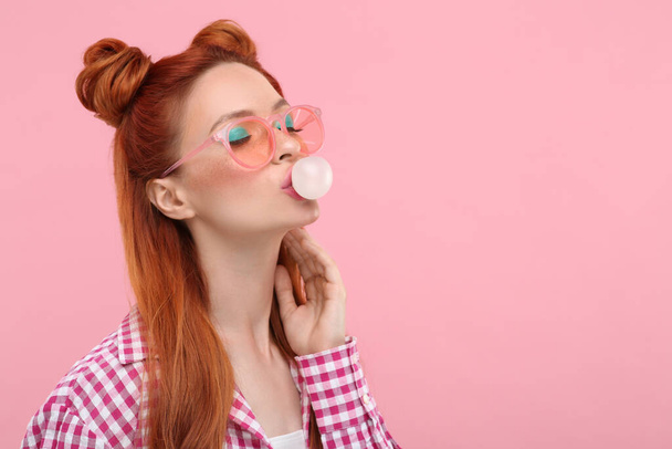 Beautiful woman with bright makeup blowing bubble gum on pink background. Space for text - Foto, Imagem