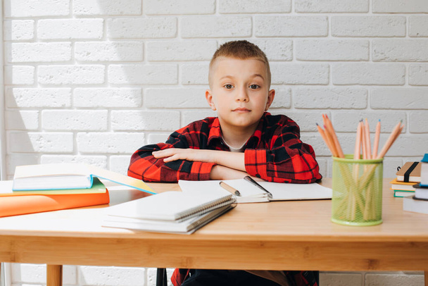 Αντίληψη πίσω στο σχολείο. Ένα αγόρι στη διαδικασία της μελέτης κάθεται σε ένα τραπέζι με unigami, σημειωματάρια και μολύβια. Πρόσθια όψη - Φωτογραφία, εικόνα