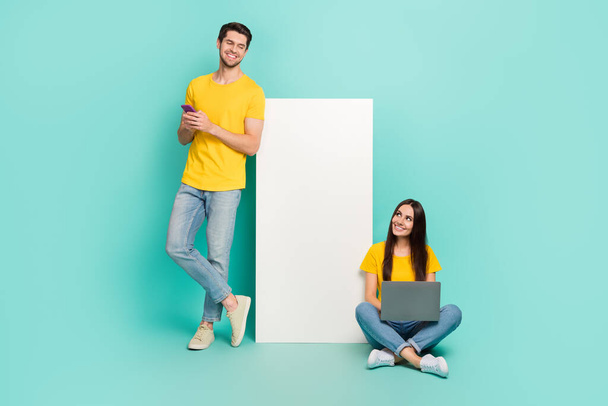 Photo of pretty dreamy married couple wear yellow t-shirts texting looking modern gadget empty space isolated teal color background. - Fotografie, Obrázek