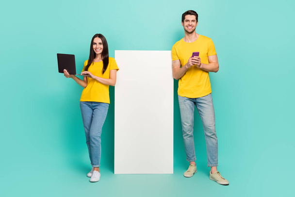 Photo of cute pretty married couple wear yellow t-shirts communicating modern gadget empty space isolated teal color background. - Fotografie, Obrázek