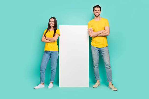 Photo of confident cute married couple wear yellow t-shirts arms crossed modern gadget empty space isolated teal color background. - Fotografie, Obrázek