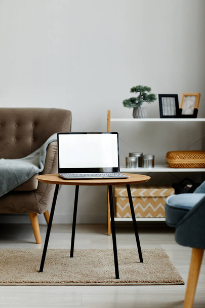 Vertical background image of opened laptop with blank white screen on coffee table in minimal living room interior, copy space - Photo, Image