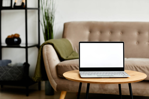 Background image of open laptop with blank white screen on coffee table in living room interior, copy space - Photo, Image