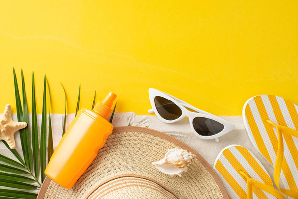 Summer Sun Essentials: Top view visueel feest voor UV Bewustzijnsmaand, met top-view SPF crème fles, zonnebril, hoed, teenslippers, schelp, zeester, en palmblad op levendig geel en zanderig doek - Foto, afbeelding
