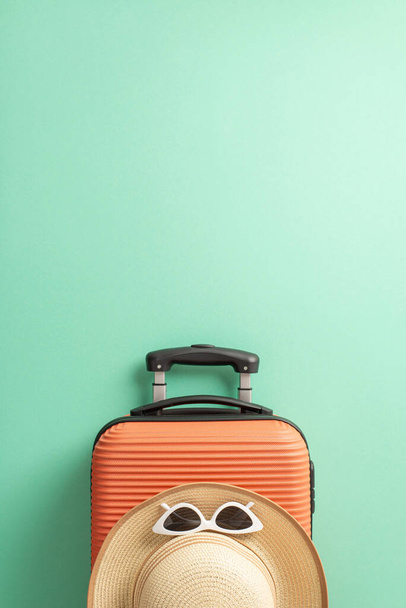 Dream vacation concept. Above view vertical photo of an orange suitcase and straw hat with white sunglasses on isolated teal background with copyspace - Photo, Image
