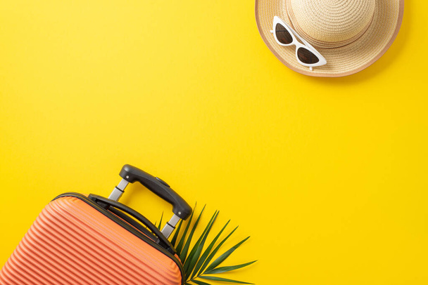 Nyári nyaralás koncepció. Felülnézeti fotó egy narancssárga bőröndről pálmalevéllel alatta és szalmakalap napszemüveggel, izolált, élénk sárga háttérrel, másolótérrel - Fotó, kép