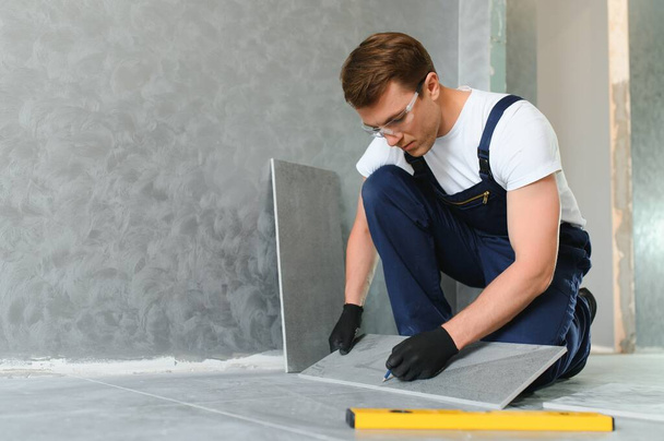 A male construction worker installs a large ceramic tile. - Foto, imagen