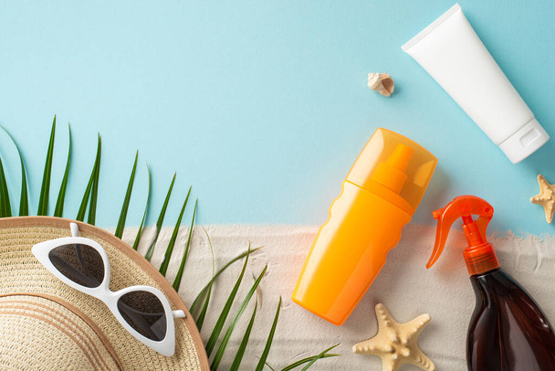 Top view arrangement of sunscreen and SPF product bottles without labels, sunglasses, sunhat, shell, starfishes, palm leaf on pastel blue and sandy surface, with vacant space for text or ad purposes - Фото, зображення