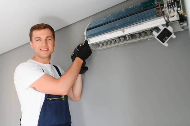 Male technician fixing air conditioner indoors. - 写真・画像