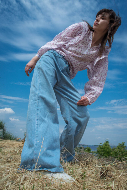 Una chica en jeans azules posa contra el cielo azul. - Foto, Imagen