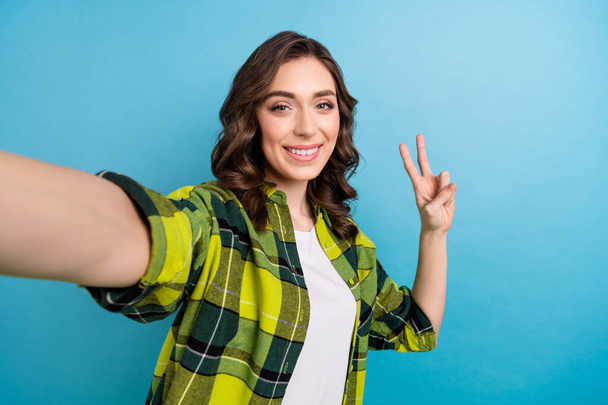 Portrait of positive cheerful cute girl wavy hairstyle wear plaid jacket doing selfie showing v-sign isolated on blue color background. - Valokuva, kuva