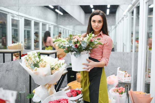 Beautiful florist at flower shop. Woman working in floral shop with copy space. Successful florist smiling. - Photo, image