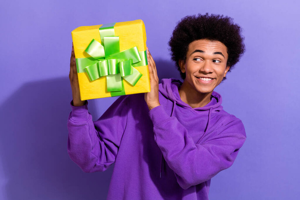 Portrait of toothy beaming person with stylish hairstyle wear violet hoodie look at present box isolated on purple color background. - Valokuva, kuva