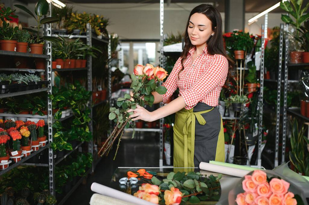 Cute girl florist collects a bouquet of roses in a flower shop. A beautiful florist creates a composition of flowers. Girl cuts flowers and removes stale leaves. - Foto, imagen