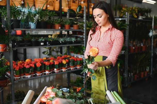 Cute girl florist collects a bouquet of roses in a flower shop. A beautiful florist creates a composition of flowers. Girl cuts flowers and removes stale leaves. - Foto, Imagen