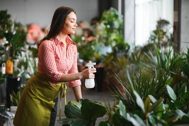 Woman florist working at her flower shop standing surrounded by plants. - Foto, imagen
