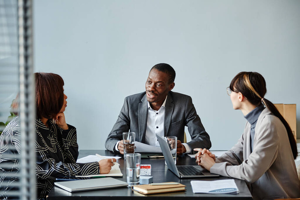 Retrato de jovem empresário negro conversando com a equipe durante reunião no escritório contra a parede azul pálida, espaço de cópia - Foto, Imagem