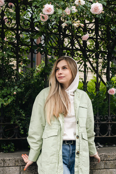 Stylish young blonde woman with long hair woman on the background of an old building with a climbing rose, urban portrait, tourism concept. - Fotó, kép