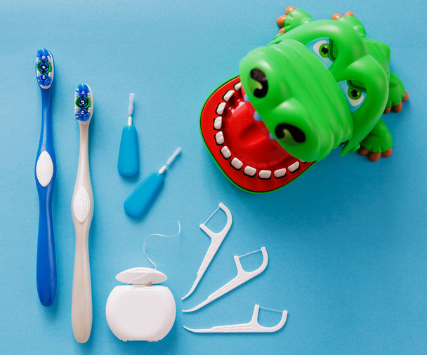 Bílá zubní nit, párátka, štětce a krokodýl na modrém pozadí - Fotografie, Obrázek