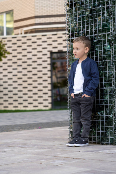 Fashion kid summer in the city stands near the wall. Trendy boy standing on the street. Vertical photo. High quality photo - Foto, imagen