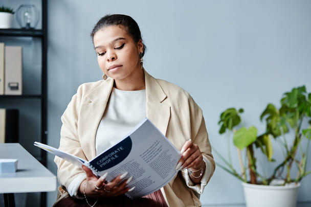 Минимальный портрет молодой черной предпринимательницы, читающей отчет на рабочем месте в офисе на сером фоне, копировальное пространство - Фото, изображение