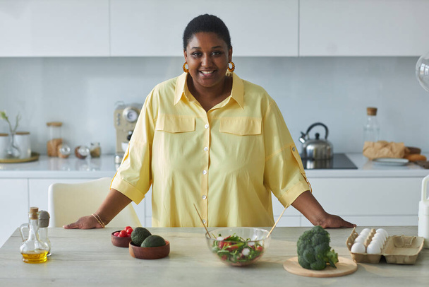Portret Afroamerykanki uśmiechniętej do kamery podczas przygotowywania jedzenia w kuchni - Zdjęcie, obraz