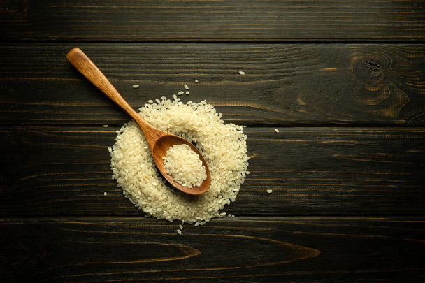 Grumos brancos de arroz espalhados em uma mesa vintage e em uma colher de madeira. O conceito de cozinhar mingau de arroz na cozinha. Espaço preto para menu ou receita. - Foto, Imagem