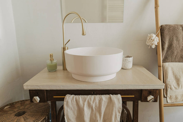 Modern fürdőszoba belső. Modern kerámia mosogató arany csap rusztikus állvány szappannal és létrával törölközővel a háttérben a fal tükörrel. Stílusos boho fürdőszoba design. - Fotó, kép