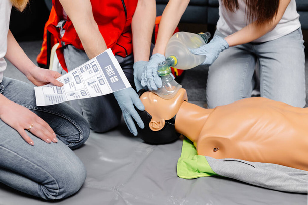 Frau mit Atemschutztasche Ambu bag. Vorführung der CPR Herz-Lungen-Wiederbelebung Ausbildung medizinischer Verfahren an der CPR-Puppe in der Klasse. Sanitäter demonstrieren Erste-Hilfe-Praxis zur Rettung von Leben. - Foto, Bild