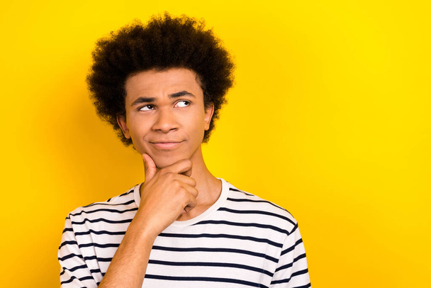 Portrait doubtful student guy look up hand on chin overthinking not sure wear striped t-shirt isolated yellow color background. - Photo, image